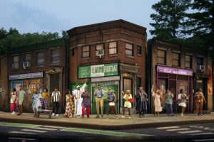 The set on an outdoor stage represents a street corner in Harlem with a laundromat, hair braiding shop, and family health center underneath windows with air conditioning units. A line of sixteen people stand on the sidewalk, dancing, raising their hands, playing the drums, and smiling.